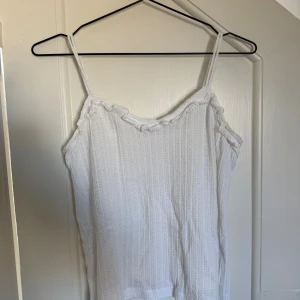 Vit linnetopp med volang från Mango - Supersöt vit linnetopp från Mango i storlek S. Toppen har tunna axelband och volangdetalj längs urringningen som kan behövas strykas lite. Den är också ribbad och har en lätt struktur i tyget, perfekt till jeans eller kjol. Luftig och skön för varma dagar!🥰
