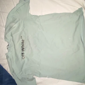 Ljusblå Off-White t-shirt med tryck - Säljer en ljusblå t-shirt från Off-White med logga framtill och stort grafiskt tryck på ryggen. T-shirten har klassisk passform och är tillverkad i mjuk bomull. Perfekt för dig som gillar streetwear och snygga detaljer.