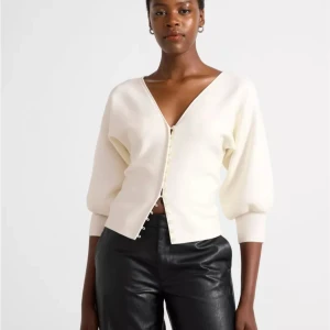 Vit kofta med v-ringning och knappar - Säljer en stilren vit kofta med djup v-ringning och pärlknappar framtill. Koftan har ballongärmar och breda muddar vid ärmslut och midja. Perfekt att styla med både jeans och kjol för en trendig look. Slutsåld i butik!💗