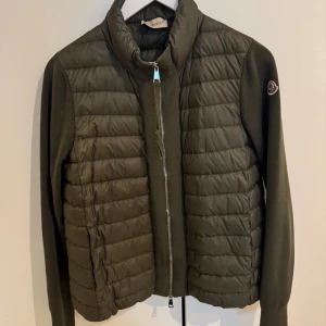 Olivgrön kofta från Moncler - Säljer min superfina olivgröna kofta från Moncler med quiltad framsida och dragkedja. Moncler-logga på ärmen och är tillverkad i en mix av dun och stickat material. Köpt på NK i Göteborg för ca 8500 SEK. 