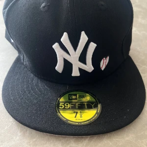 New Era Yankees 59FIFTY svart keps - Svart New Era 59FIFTY keps med New York Yankees logga i vitt framtill, broderad baseball och texten 'Love & Hustle = Game' på sidan. World Series 1996 patch i färg på ena sidan. Tillverkad i polyester, klassisk flat brim och snygg passform.