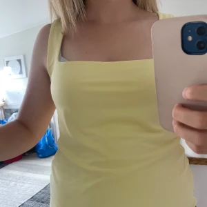 Ljusgul ärmlös klänning från Amisu - Supersöt ljusgul tröja från Amisu med fyrkantig urringning och breda axelband. Modellen är ärmlös och har en slät, enkel design som ger en fräsch och somrig vibe. Perfekt för dig som gillar stilrena plagg med lite färg.