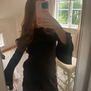 Svart ribbad tröja med trumpetärmar - Svart långärmad tröja med ribbad struktur och snygga trumpetärmar. Tröjan har en rund halsringning och är i ett stretchigt material som sitter skönt på kroppen. Perfekt för dig som vill ha en stilren men ändå trendig look.