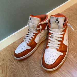 Nike Air Jordan 1 Orange/Vit US10 - Nike Air Jordan 1 sneakers i orange och vitt skinn med klassisk svart Air Jordan-logga på sidan. Skorna har vita snören, perforerad tå och orange meshfoder. Snygg kontrast mellan de vita och orangea panelerna, perfekt för dig som vill sticka ut.