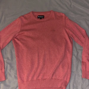 Rosa stickad tröja från Barbour S - Säljer en rosa stickad tröja från Barbour i storlek S. Tröjan har rund halsringning, ribbade muddar och diskret broderad Barbour-logga på bröstet. Perfekt för dig som gillar klassisk och stilren design.