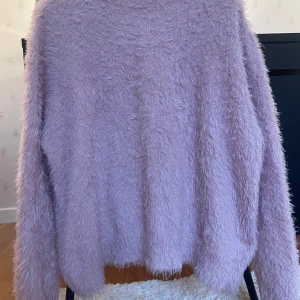 Rosa fluffig stickad tröja - Supermjuk och fluffig stickad tröja i rosa. Tröjan har lång ärm och en avslappnad passform. (Har en liten grå fläck som knappast syns) 