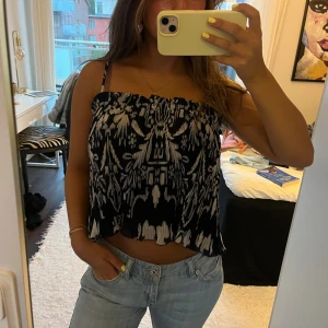 Mörkblå och vit mönstrad linnetopp - Säljer en mörkblå och vit linnetopp med unikt grafiskt mönster. Toppen är croppad med tunna axelband och har en lätt rynkad kant nertill. Endast använd en gång 