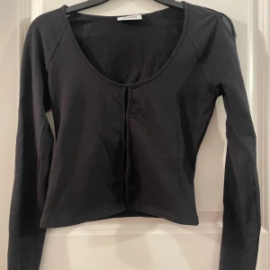 Svart långärmad topp från Weekday - Svart långärmad topp från Weekday i modellen Nicolina Long Sleeve. Toppen har en djup rundad ringning, dekorativa slitsar framtill och längs ärmarna samt en croppad passform. Tillverkad i mjuk bomull med en clean och stilren look.