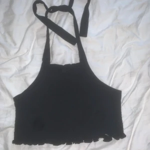 Svart halterneck-topp - Svart halterneck-topp från Collusion med knytband i nacken och volangkant nedtill. Toppen är ärmlös och har en enkel, stilren design som passar perfekt till sommaren. 