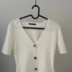 Vit blus med hjärtformade knappar Gina Tricot - Supersöt vit blus från Gina Tricot med v-ringning och korta ärmar. Blusen har unika hjärtformade knappar framtill som ger en gullig touch. Perfekt att styla med jeans eller kjol för en fräsch look.
