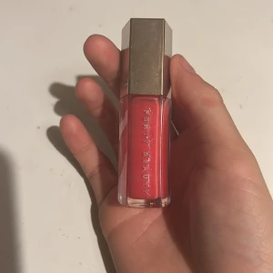 Fenty Beauty rött läppglans - Snyggt rött läppglans från Fenty Beauty med glansig finish. Kommer i en stilren, genomskinlig fyrkantig tub med silvrigt lock i femkantig form och Fenty-logga på toppen. Perfekt för dig som vill ha en poppig färg på läpparna.