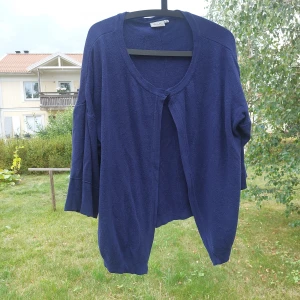 Mörkblå kofta från Dea, storlek XL - Mysig mörkblå kofta från Dea i storlek XL. Koftan har en enkel design med rund halsringning och en knapp framtill. Den är stickad och har långa ärmar med en loose passform, perfekt att slänga på sig när det är kyligt ute.
