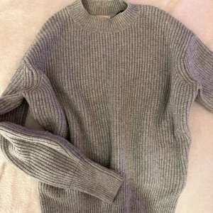 Grå ribbstickad tröja från H&M - Mysig grå ribbstickad tröja från H&M i storlek XS. Tröjan har hög hals och långa ärmar, perfekt för kyliga dagar. Den är stickad i ett mjukt material och har en klassisk, enkel design som är lätt att matcha med allt.