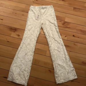 Vita blommiga byxor från NA-KD - Superfina vita byxor från NA-KD med blommigt broderat mönster och lätt utsvängda ben. Byxorna har hög midja och elastisk linning för skön passform. Perfekta för dig som vill sticka ut med en unik och trendig look.