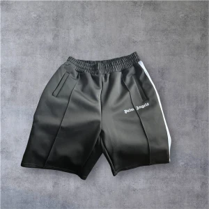 Svarta shorts från Palm Angels - Palm Angels svarta shorts med vit sidoremsa och logga på vänster ben. De har elastisk midja och två fickor fram. Sportig vibe och loose fit, perfekta för chill eller streetwear. Materialet känns som polyester och har en lätt glans.