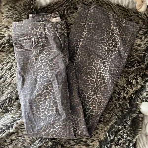 Leopardmönstrade jeans från Nelly - Snygga jeans från Nelly med leopardmönster i grå och beige toner. Byxorna har klassisk femficksdesign, dubbla knappar i midjan och bälteshällor. Perfekta för dig som vill sticka ut med ett djurmönstrat statement.
