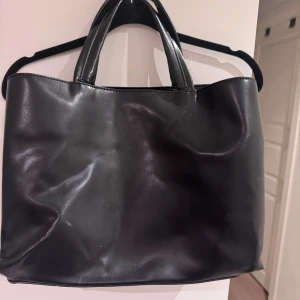 Svart väska  - Fin väska perfekt för skola eller jobb. Har tre större fack där ett av dom är perfekt för en mindre dator/ipad. Medföljande band för att ha den som en cross-body väska