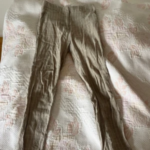 Beige randiga linnebyxor från Mango - Snygga beige linnebyxor från Mango med tunna vita ränder. Byxorna har normal passform, hällor för bälte och raka ben. Perfekta för en chill och stilren look under varmare dagar.