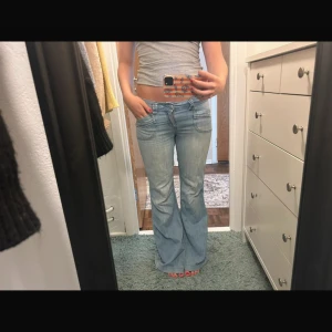 Ljusblå bootcut jeans från Orsay - Ljusblå jeans från Orsay med bootcut-modell och låg midja. Snygga detaljer med markerade sömmar och stora fickor fram och bak. Jeansen är i klassisk denim och har dragkedja och knapp framtill. Perfekta för dig som gillar retrovibbar och en avslappnad look.