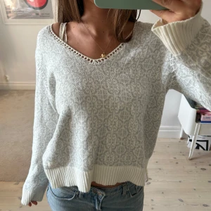 Ljusgrå Odd Molly tröja med broderi - Superfin ljusgrå stickad tröja från Odd Molly med diskret mönster, v-ringning med virkade detaljer och broderad ros med texten 'Rise Above' på ryggen. Ribbstickade muddar och avslappnad passform. 