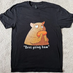 Svart t-shirt med hamstertryck - Svart t-shirt med ett roligt tryck av en tecknad hamster som äter och texten 'Bros going ham' på framsidan. Klassisk passform med rund hals och korta ärmar. Perfekt för dig som gillar humor och vill sticka ut lite extra.