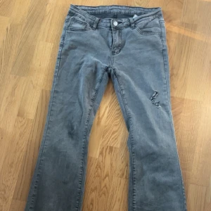 Grå bootcut jeans med slitning - Grå jeans med bootcut passform och snygg slitning på ena benet. Klassisk femficksmodell med knapp och dragkedja. Perfekta för dig som gillar en avslappnad men trendig look. Knappt använd 