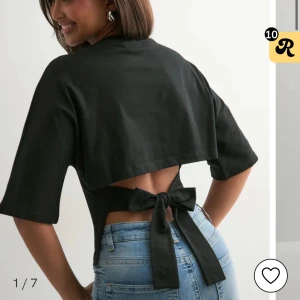 Svart topp med knyt i ryggen - Snygg svart bolerotopp med öppen rygg och breda knytband som knyts i en rosett bak. Toppen har halvlånga ärmar och croppad passform, perfekt till höga jeans. Enkel och stilren design som sticker ut.