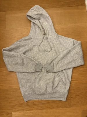 Grå hoodie från Bikbok, Storlek XS - Tjock grå hoodie från bikbok i storlek XS. Två fickor fram och snörning fram. Perfekt till svarta byxor och även jeans. 60% Polyester, 40% Bomull.