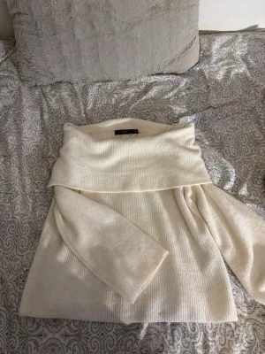 Vit ribbad offshoulder stickad tröja - Säljer en vit stickad tröja från Vero Moda i storlek L. Tröjan har en bred offshoulder-krage och är ribbstickad för en snygg struktur. Perfekt för kyliga dagar och enkel att styla med dina favoritjeans.