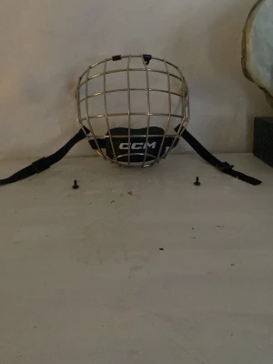 Ingen väst – hockeygaller CCM FM580 S - Det här är ett hockeygaller från CCM, modell FM580 i storlek S. Gallret är i metall med svart hakskydd och justerbara remmar. Perfekt för dig som vill skydda ansiktet på isen. Skruvar för montering medföljer.  Använd 1 gång. 