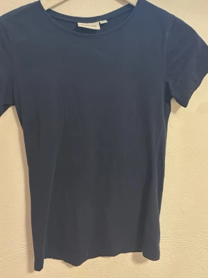 Mörkblå t-shirt från Kappahl XS - Enkel och stilren mörkblå t-shirt från Kappahl i storlek XS. Klassisk rund halsringning och korta ärmar. Tillverkad i mjuk bomull som känns skön mot huden. Perfekt basplagg till alla outfits.