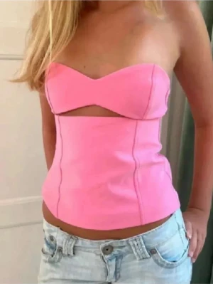 Rosa bandeau tubtopp med cut-out - Säljer en snygg rosa bandeau tubtopp med en cool cut-out detalj under bysten. Toppen är axelbandslös och har en figurnära passform som framhäver midjan. Perfekt för sommarens alla tillfällen och passar till både jeans och kjol.