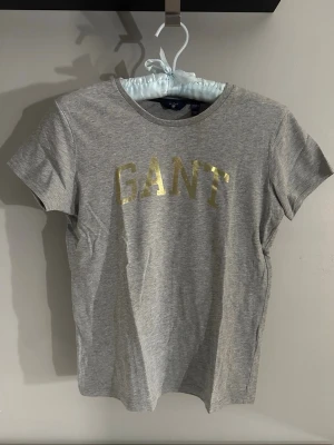 Grå Gant T-shirt  - Grå Gant t-shirt med guldtryck i stl. 158/164 (13-14år)