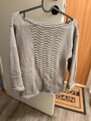 Beige stickad tröja med vågmönster - Säljer en beige stickad tröja med vågigt hålmönster framtill. Tröjan har bred halsringning och trekvartsärm, perfekt för lager på lager och chill stil. Passar till både jeans och kjol för en avslappnad vibe.