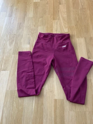 Vinröda leggings från Stronger - Snygga vinröda leggings från Stronger med hög midja och tight passform. Tillverkade i ett stretchigt syntetmaterial som passar perfekt till träning. Diskret logga på höften och meshdetaljer på benen för extra stil.