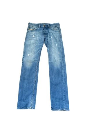 Diesel Belther ljusblå jeans straight fit - Säljer ett par ljusblå Diesel Belther jeans med slitna detaljer och raka ben. Jeansen har klassisk femficksdesign, låg midja och är tillverkade i slitstarkt denim. Snygg faded effekt och diskreta slitningar för en avslappnad look.
