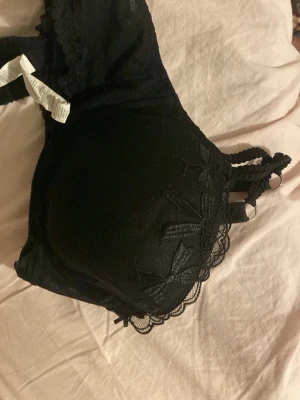 Svart spets-bh med broderade detaljer intissimi  - Säljer en svart bh med vadderade kupor och broderade spetsdetaljer. Axelbanden är dubbla och flätade för en extra snygg look. Bh:n har fina blommiga broderier och en elegant kant i spets. Perfekt för dig som gillar stilrena underkläder med det lilla extra. Bh-n är från intimissmi