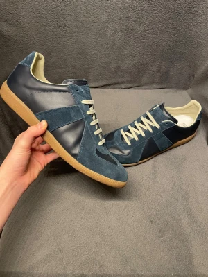 Margiela gats - Säljer ett par snygga gats från Maison Margiela i mörkblått skinn och mocka med beige snörning och gummisula. Klassisk rund tå och platt sula, perfekt för dig som gillar stilrena och coola skor med retrovibe. Aldrig använda. Nypris runt 8000. Skriv vid frågor, priset är inte hugget i sten🤝