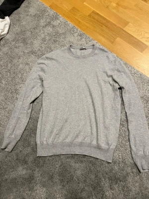 Grå tröja från Max Tonso i cashmereblandning - Säljer en stilren grå tröja från Max Tonso i storlek M. Tröjan är tillverkad i en mjuk mix av 95% bomull och 5% cashmere, har rund halsringning och långa ärmar. Perfekt för dig som gillar en clean och enkel look. storlek M passar S