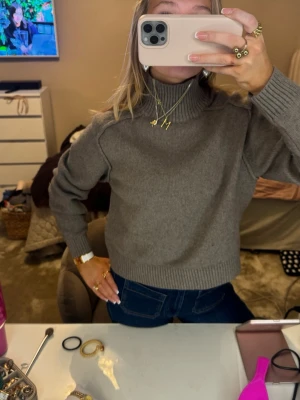 Grå polotröja i stickad ull - Säljer en grå polotröja i stickad ull med ribbade muddar och hög krage. Tröjan har en klassisk, lite loose passform och är perfekt för kyliga dagar. Enkel att matcha med jeans eller kjol för en chill och snygg look.