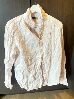 Ljusrosa linneskjorta från Polo Ralph Lauren - Säljer en ljusrosa skjorta från Polo Ralph Lauren i linne med klassisk krage och knappar framtill. Skjortan har lång ärm och den ikoniska broderade loggan på bröstet. Perfekt för dig som gillar en avslappnad men ändå stilren look.