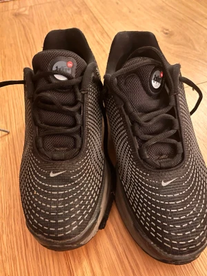 Svarta Nike Air Max sneakers - Säljer ett par svarta Nike Air Max sneakers med vitmönstrad ovandel och klassisk Nike-logga på tån. Skorna har snörning och meshmaterial för bra ventilation. Snygg och sportig design som passar till många olika outfits.