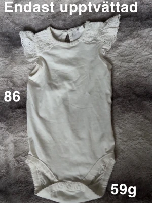 Vit body med spetsärmar - Söt vit body med fina spetsdetaljer på axlarna. Rund halsringning och tryckknappar i grenen för enkel påklädning. Perfekt för dig som gillar romantiska detaljer och stilren look.🌸 Oanvänd endast upptvättad. Storlek 86