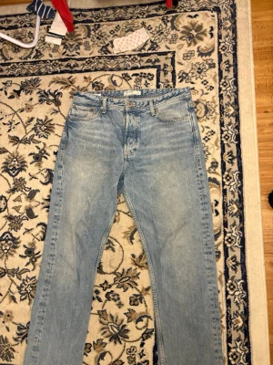 Ljusblå jeans från Jack & Jones - Säljer ett par ljusblå jeans från Jack & Jones med klassisk femficksdesign och raka ben. Jeansen har en snygg tvättad look, metallknapp med logga och läderpatch bak i midjan. Tillverkade i bomullstyg som känns skönt och slitstarkt.