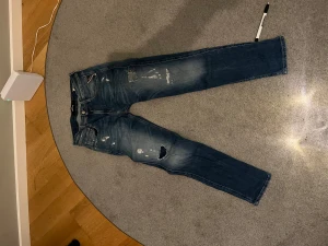 Replay blå slitna jeans, midwaist - Säljer ett par blå jeans från Replay med snygga slitningar och hål på benen. Strl w28 L30. Jeansen har klassisk femficksdesign, normal passform och är tillverkade i jeansmaterial. Perfekta för dig som gillar en lite ruffare streetstil.