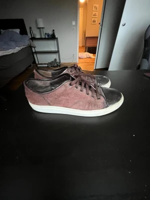 Lanvin cap toe - Säljer ett par bruna sneakers med snygga mockadetaljer på sidorna och blanka skinnpartier vid tån. Skorna har rund tå, snörning och vit platt sula. Perfekta för dig som gillar en chill och stilren look.