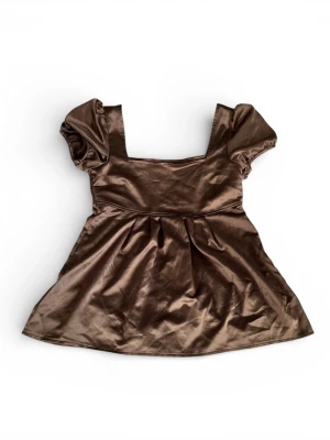 Brun satinblus med puffärm - Supersöt brun blus i glansigt satinmaterial med puffiga korta ärmar och fyrkantig ringning. Bra skick förutom att det är nopprig på vissa ställen (kan ses på 3 sista bilderna). Tröjan är i storlek xs och har en löspassform.