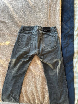 Grå mönstrade jeans från Jacob Cohen - Säljer ett par grå jeans från Jacob Cohen i storlek 31. Byxorna har ett diskret mönster, klassisk femficksdesign och normal passform. Materialet är en blandning av bomull och syntet vilket gör dem både bekväma och snygga. Perfekta för dig som vill ha något unikt i garderoben.