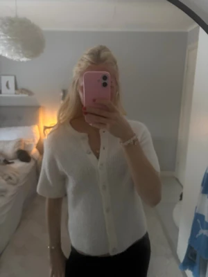 Vit kortärmad kofta med knappar - Säljer en söt vit kofta med korta ärmar och knappar framtill. Koftan är stickad och har en enkel, clean look som passar perfekt till de mesta. Endast använd 1 gång och köptes på Gina för ca 1 år sen. 