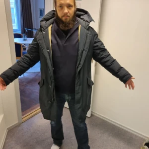 Woolrich Svart parkajacka med huva - Säljer en svart woolrich parkajacka med stor huva och dragkedja framtill. Jackan har långa ärmar, två stora fickor med lock och knappstängning samt en clean, rak passform. Perfekt för kalla dagar och har en snygg, enkel look som funkar till jeans och hoodie. Nypris 10000kr